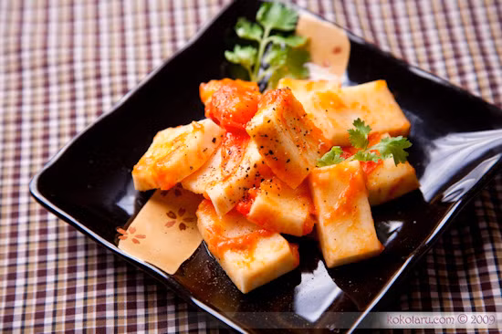 Phi thơm hành cùng với cà chua, khi cà chua nhừ thì cho một ít nước mắm, hạt nêm vào đảo đều rồi cho dừa vào om cùng. Đun lửa nhỏ cho tới khi nước cạn gần hết, miếng dừa ngấm đều với gia vị là được, rồi trộn ớt và hành tươi vào bắc xuống, cho ra đĩa. Ảnh: Kokotaru.com.