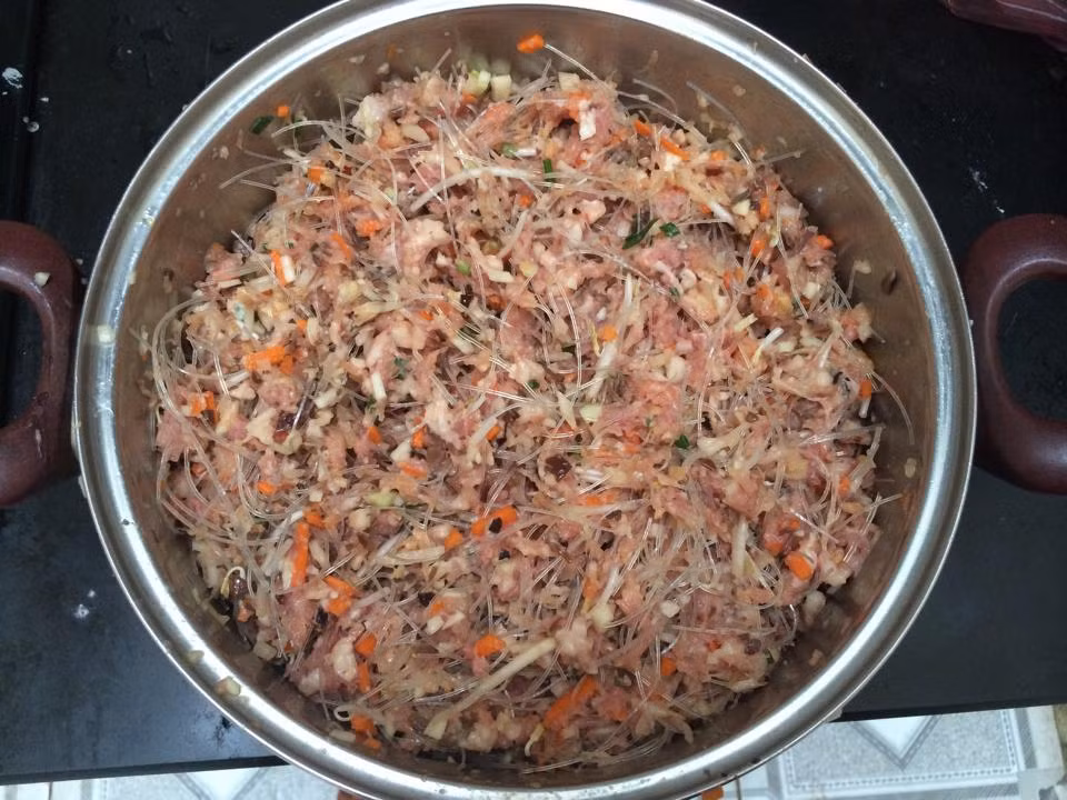 Cho tất cả các nguyên liệu: thịt, tôm, đậu xanh, trứng gà, hành tây, cà rốt, khoai môn, mộc nhĩ đã xào vào một tô lớn. Nêm cùng với muối, đường, hạt nêm, hạt tiêu và tỏi băm nhuyễn. Sau đó trộn đều.