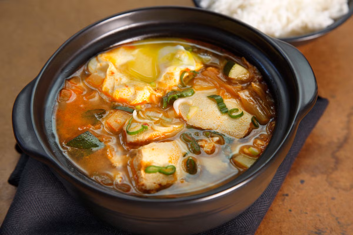 Canh kim chi đậu phụ. Đây là một trong những món ngon dễ làm từ kim chi bạn có thể thực hiện tại nhà. Cho hành tươi (phần trắng và xanh nhạt) vào xào cùng muối trong khoảng 5 phút để dậy mùi. Sau đó, cho bí ngòi thái lát vào, nêm gia vị và đảo đều. Thêm kim chi, nước dùng từ gà, xì dầu và đun sôi. Cho các tảng đậu vào, cẩn thận không để đậu vỡ ra. Nêm ném gia vị cho vừa miệng, dọn ra bát và dùng nóng. Ảnh: CHOW.
