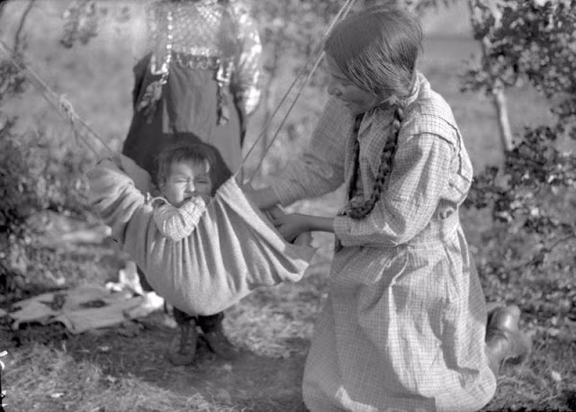 Bé gái chơi đùa với em nhỏ ngồi trên võng ở Bắc Saskatchewan, miền tây Canada, hàng chục năm trước. Ảnh: VT.