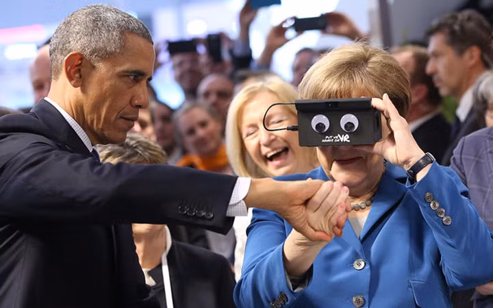 Bà Merkel tỏ ra thích thú khi được ông Obama giới thiệu loại kính thực tế ảo có thiết kế vui nhộn. Ảnh: DPA