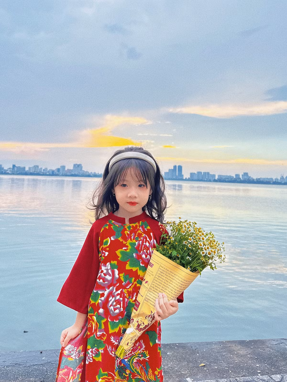 Cô bé được diện cho chiếc áo dài họa tiết chăn con công nổi bật, đeo bờm dịu dàng, ôm bó hoa cúc tana. Ảnh: Vietnamnet