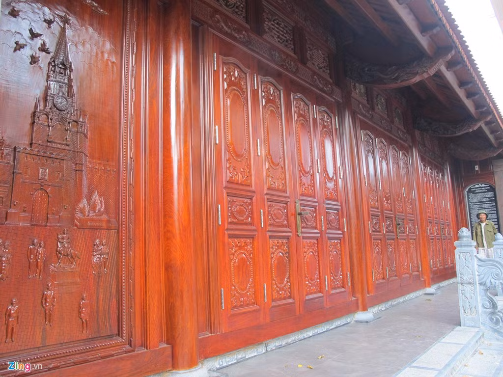 Ngay từ lúc bước vào cổng, mọi người sẽ bị choáng ngợp bởi hai cánh được làm từ hai tấm gỗ nguyên khối, mỗi tấm dày 10 cm, cao 2,5 m, rộng 1,2 m. Xung quanh cổng trang trí đèn màu bắt mắt. phía trên ghi dòng chữ: Nhà Lưu niệm gia đình ông Trần Quang Chưởng và bà Nguyễn Thị Nhiên. Ảnh: Zing.