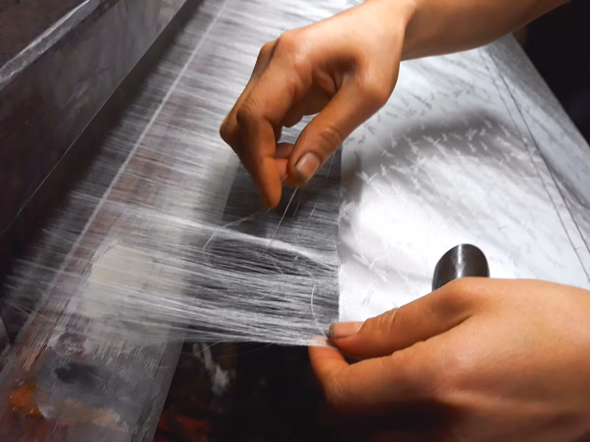 Một công nhân thực hiện công đoạn rút tơ thừa trước khi dừng dệt.