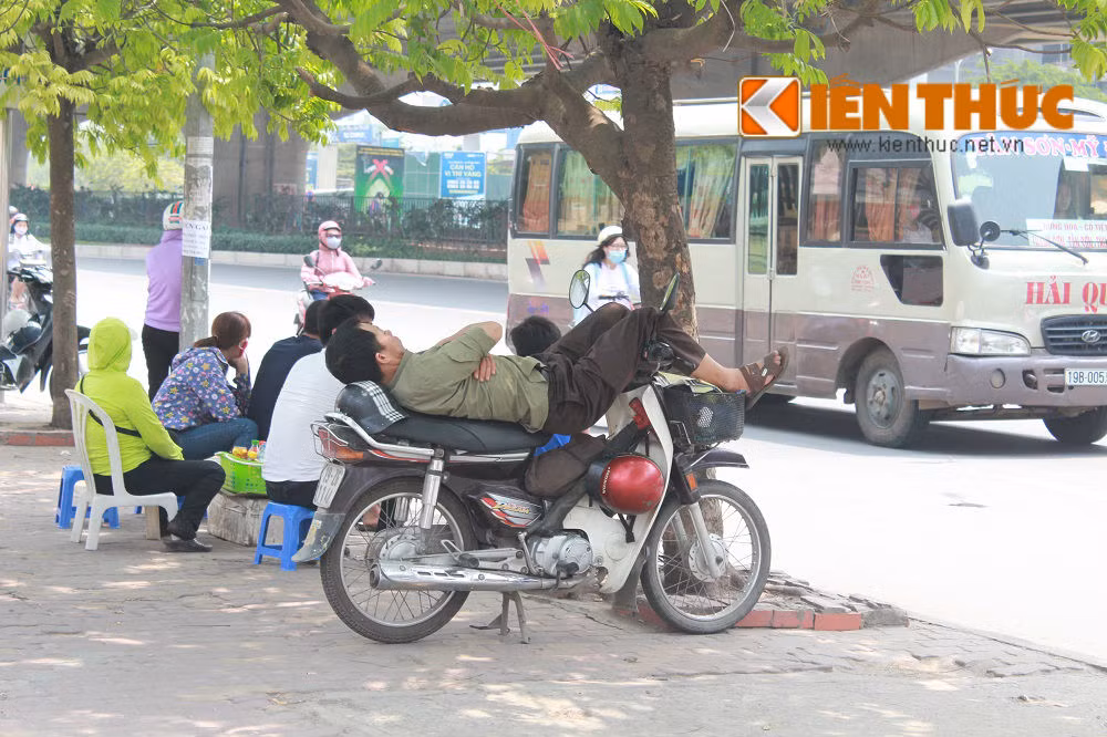 Một bác xe ôm tranh thủ nằm nghỉ dưới gốc cây