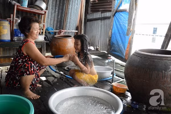 Bà Nguyễn Thị Hai (57 tuổi) đang tắm cho cháu. Bà chia sẻ trên Afamily: "Cuộc sống trong khu ổ chuột này thiếu thốn đủ bề. Nước sạch khan hiếm nên có khi phải dùng nước tạm dưới sông. Nhà luôn bị dột, mỗi lần có gió hơi lớn là tốc mái. Nhà tôi bị tốc mái nhiều lần rồi, mỗi lần như vậy phải mua tôn cũ nát về che chắn tạm" - Ảnh nguồn: Afamily.