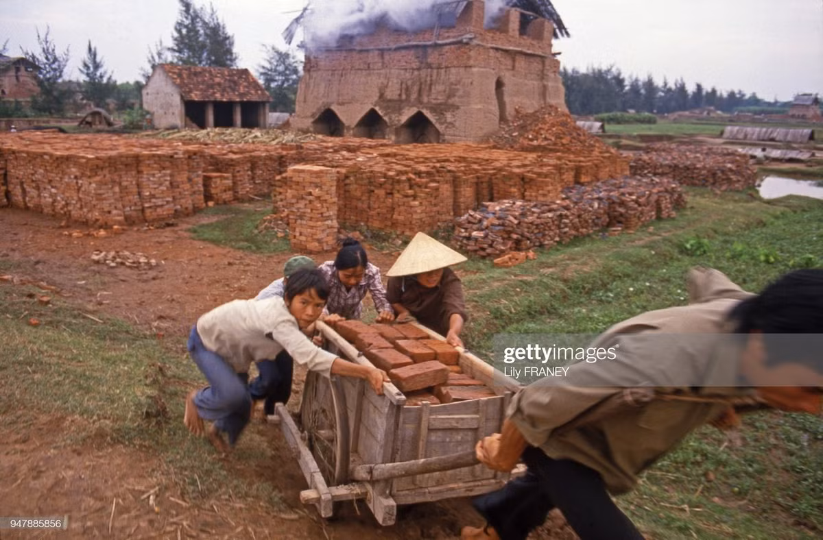 Cậu bé phụ người lớn đẩy xe chợ gạch tại một lò gạch.