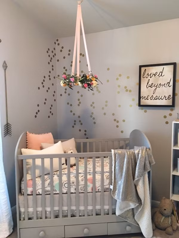 Thông thường, nội thất chính của phòng trẻ sơ sinh sẽ là chiếc cũi xinh xắn. Bạn có thể lựa chọn cũi có cùng tông màu với rèm hoặc màu sơn tường. Không cần trang trí cầu kỳ, không gian của bé vẫn đẹp dịu dàng với họa tiết chấm bi trên tường và đồ treo nôi hình hoa xinh xắn.