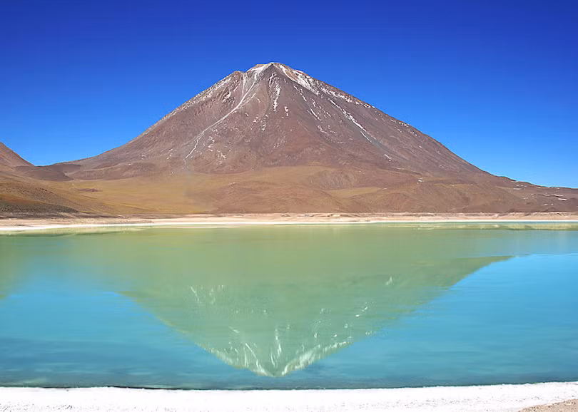 10. Laguna Verde Laguna Verde, một hồ nước mặn, nằm ở phía tây nam của đồng bằng cao của Bolivia. Đối với những người nói tiếng Tây Ban Nha, sẽ không có gì ngạc nhiên trước vẻ đẹp của hồ nước với tên gọi Laguna Verde (Đầm xanh) này. Hồ có một màu xanh tuyệt vời. Nằm dưới chân núi lửa Licancabur, màu xanh lá cây tươi đẹp của nước hồ cộng hưởng với màu vàng đồng của ngọn núi tạo thành một khung cảnh nên thơ.