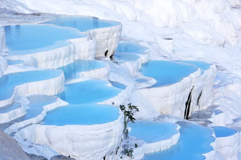 Lâu đài Bông “Cotton Castle” Pamukkale là một địa điểm check-in không thể bỏ lỡ khi đặt chân tới Thổ Nhĩ Kỳ. Nhìn từ xa, Pamukkale trắng xóa cứ như một ngọn núi tuyết, nơi đây được hình thành từ một dạng trầm tích lắng đọng do nước từ các suối nước nóng chứa nhiều canxi cacbonat chảy qua các gờ đá trong nhiều niên kỷ, tạo nên chuỗi những nhũ đá vôi trắng tinh xếp lớp như vỏ sò.