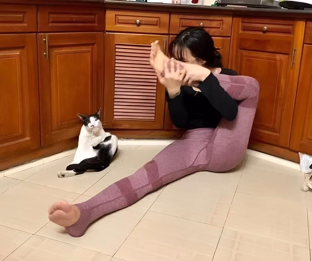 Trong ảnh, cô gái đang tập một số động tác yoga tại nhà, bên cạnh là chú mèo với bộ lông đen trắng.