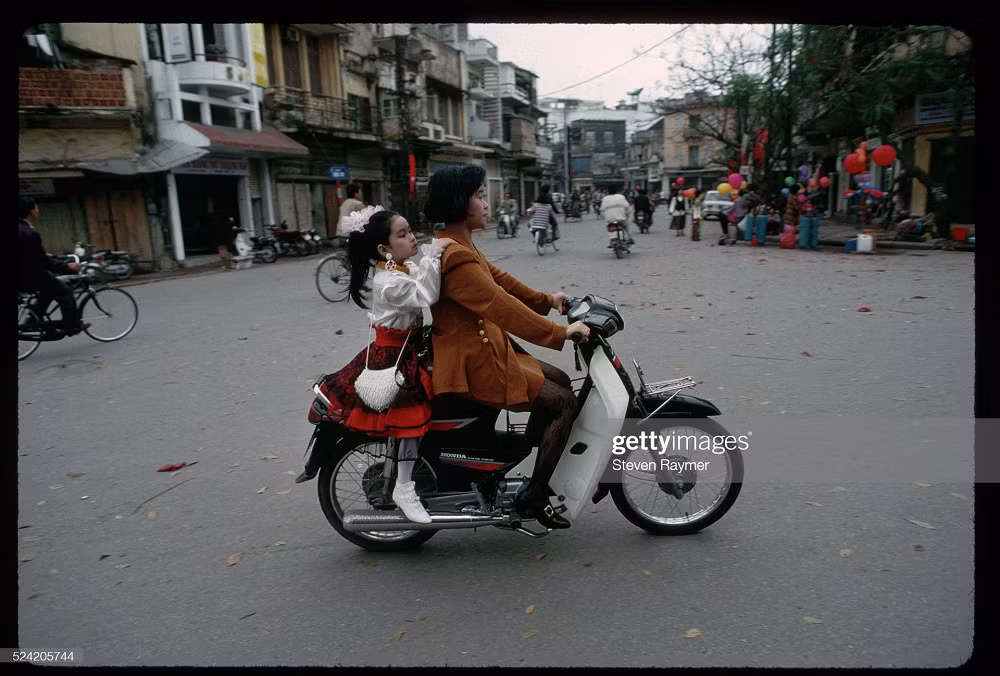 Trên một con phố ở Hà Nội, bà mẹ đèo cô con gái xúng xính trong bộ váy áo mới ngày Tết, đường sá thưa thớt người và những căn nhà mang một màu cổ kính. Ảnh: Steven Raymer.
