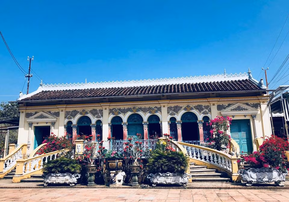 Bước qua rào cổng kiên cố bằng bê tông và sắt theo kiểu dinh thự Pháp, ngôi nhà cổ Bình Thủy nổi bật trên một khoảng sân rộng, được bao bọc bởi chùm hoa đủ màu, các chậu cây cảnh quanh năm xanh tốt làm không gian vừa có sẵn nét cổ kính, vừa sống động, tươi mới.