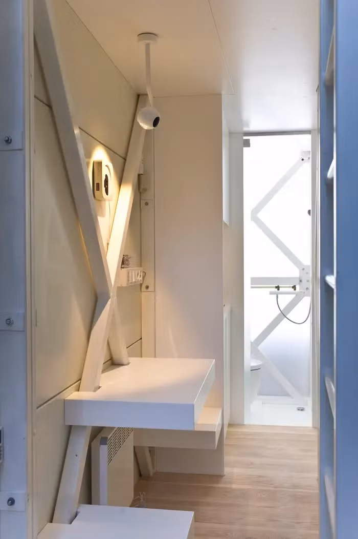 Phía sau khu vực tiếp khách là căn bếp nhỏ với bồn rửa, bếp nấu và tủ lạnh mini, xa hơn là phòng tắm nhỏ có vòi sen.