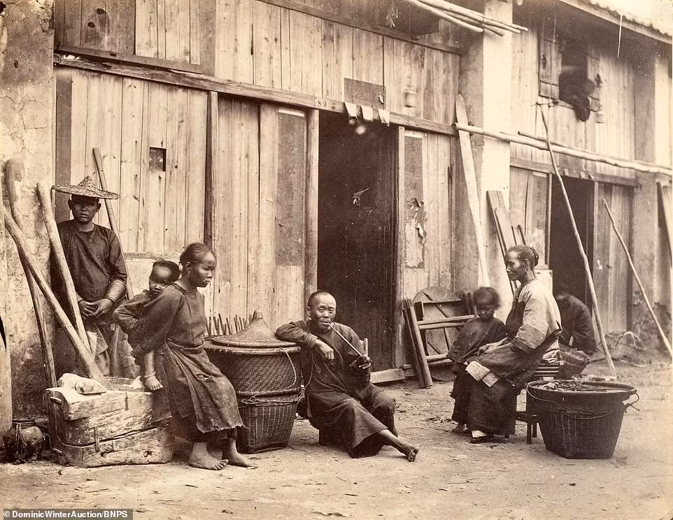 Một số cư dân ngồi bên ngoài nhà, có người không ngại nhìn thẳng vào ống kính nhiếp ảnh gia Thomson.