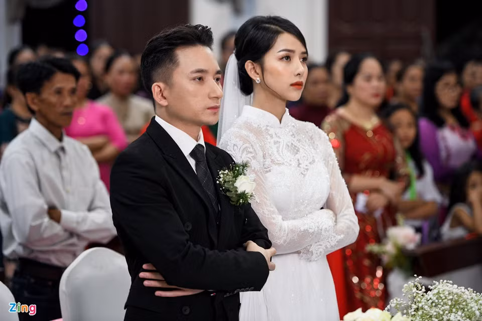 Trong thánh lễ hôn phối, nhạc sĩ Mắt biếc diện suit đen lịch lãm. Đứng cạnh anh, Huỳnh Khánh Vy mặc áo dài trắng được thiết kế tinh tế. Cả hai khoanh tay, thực hiện các nghi thức của buổi lễ.
