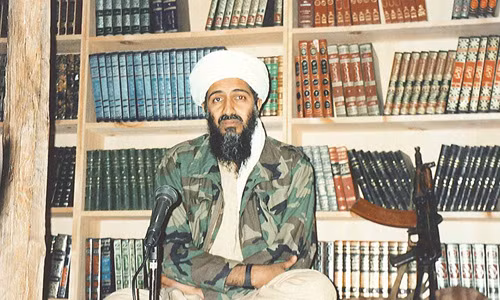 Trùm khủng bố bin Laden chuẩn bị bài phát biểu bên cạnh 1 khẩu súng và giá sách Hồi giáo.