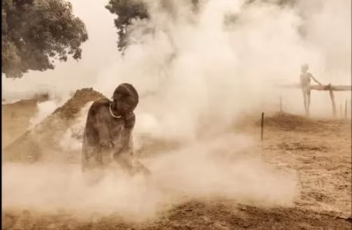 Một phụ nữ Mundari dọn sạch phân trên mặt đất trước khi đàn gia súc từ đồng cỏ trở về nhà. Phụ nữ bộ tộc cũng làm công việc vắt sữa động vật và chăm sóc con cái.