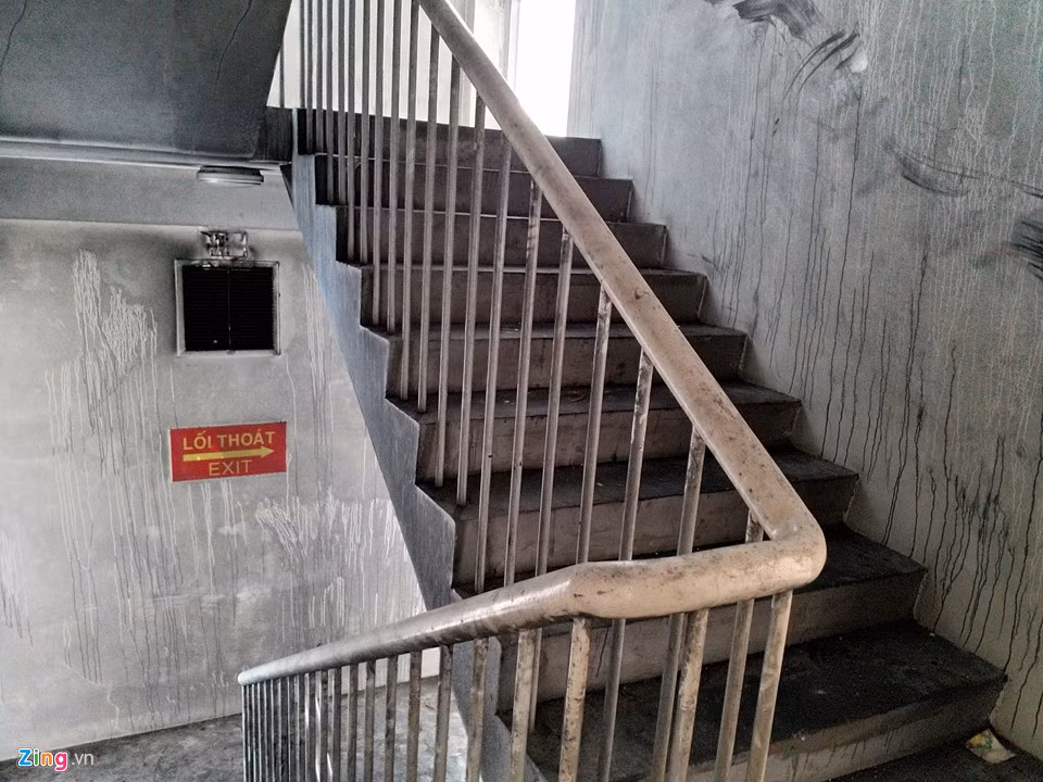 Gần 20 ngày sau vụ cháy tại chung cư Carina Plaza, cầu thang khu nhà block A, nơi thiệt hại nhiều nhất, vẫn đen kịt vì khói. Những mảng tường ám muội than, không khí nặng mùi cháy khét, khói bụi, và rác thải để lâu ngày. Khu nhà này đang được dọn dẹp. Không còn bảo vệ nào ở đây.