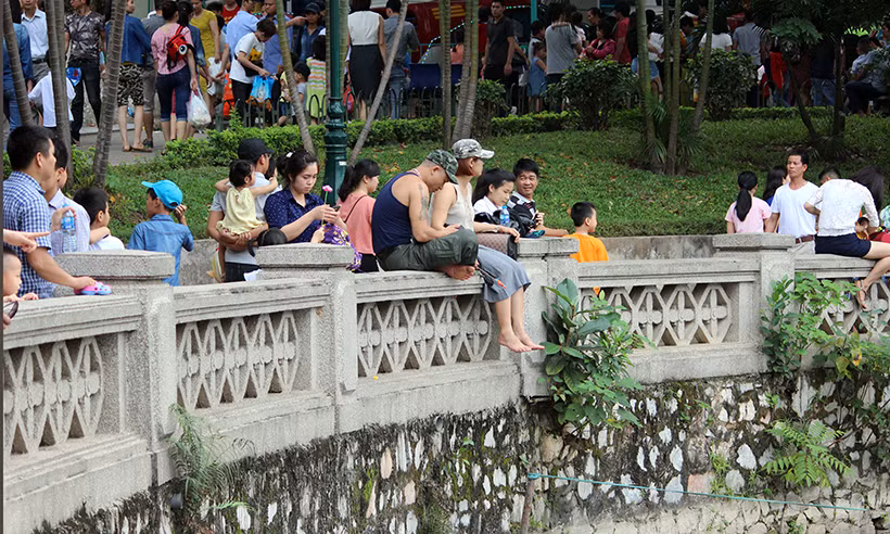 Cả nam lẫn nữ ngồi vắt vẻo trên thành hồ nước trong công viên...