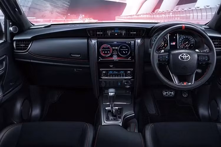 Bước vào trong cabin, Toyota Fortuner GR Sport 2024 chào đón người dùng với không gian nội thất mang tông màu đen chủ đạo với điểm nhấn màu bạc, đường chỉ khâu màu đỏ trên một số chi tiết. Hệ thống ghế ngồi được bọc da đen, đục lỗ. Tương tự, vô lăng của xe cũng được bọc da, có điểm nhấn màu đỏ cùng logo GR, tích hợp các phím chức năng và có thể điều chỉnh 4 hướng.