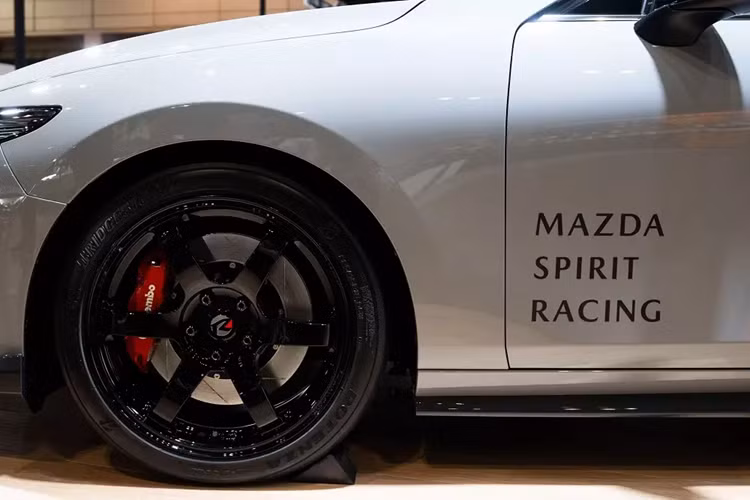 Chưa hết, Mazda Spirit Racing 3 Concept còn có những chi tiết trang trí màu đỏ nổi bật trên cản trước và vỏ gương chiếu hậu. Phía sau bộ vành la-zăng 6 chấu màu đen bóng khỏe khoắn của xe cũng là cùm phanh sơn màu đỏ. Ngoài ra, xe còn mang trên mình màu sơn ngoại thất xám xi măng tuy không nổi bật nhưng vẫn khá ấn tượng.