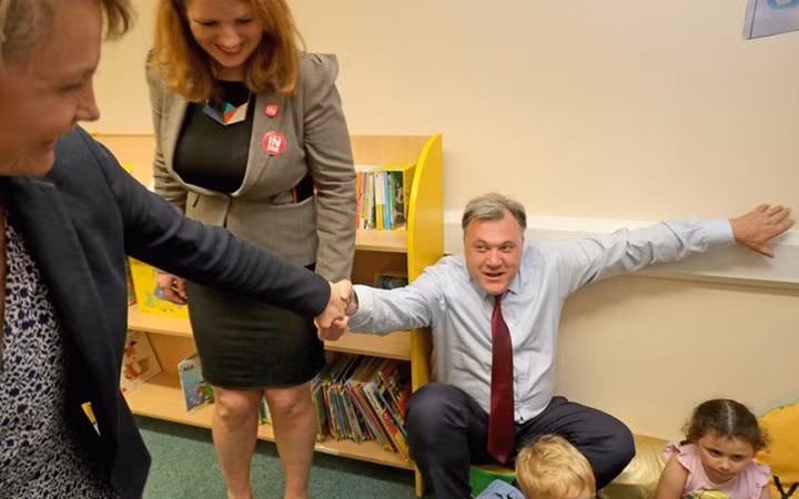 Nghị sỹ Anh Ed Balls lúng túng khi phải phải nhờ vợ kéo đứng dậy sau một buổi đọc chuyện cho các em nhỏ.