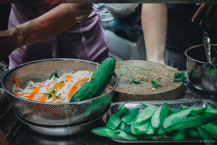 Một ổ bánh mì có các loại dưa chua, dưa leo, hành ngò, với 5 viên thịt nướng cùng nước sốt đậm đà.