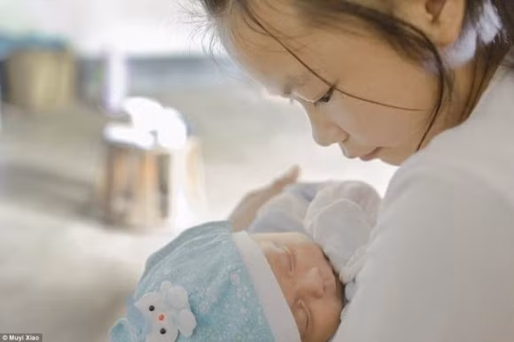 Xiao Cai 16 tuổi bế đứa con 2 tháng tuổi tại ngôi làng Quảng Đông, tỉnh Vân Nam, Trung Quốc. Xiao Cai đã kết hôn được một năm. Cô bỏ học từ khi 11 tuổi vì không đủ điều kiện theo học.