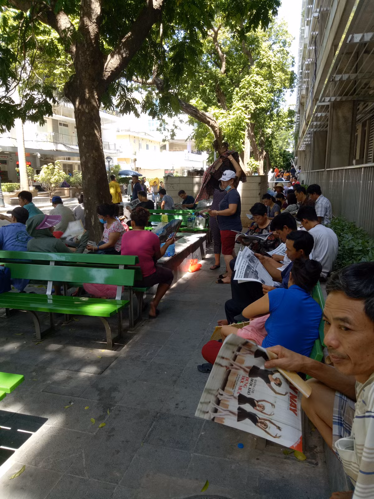 Ở khu ngoài trời, nhiều người nhà bệnh nhân mua tờ báo để vừa đọc, vừa là công cụ quạt mát.