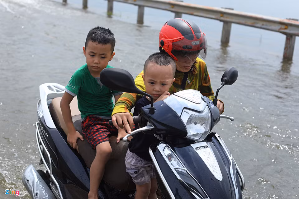 Một phụ nữ chở hai em bé xe bị chết máy phải dắt bộ chặng đường khá dài. Những đoạn ngập sâu chị cũng bị loạng choạng tay lái.