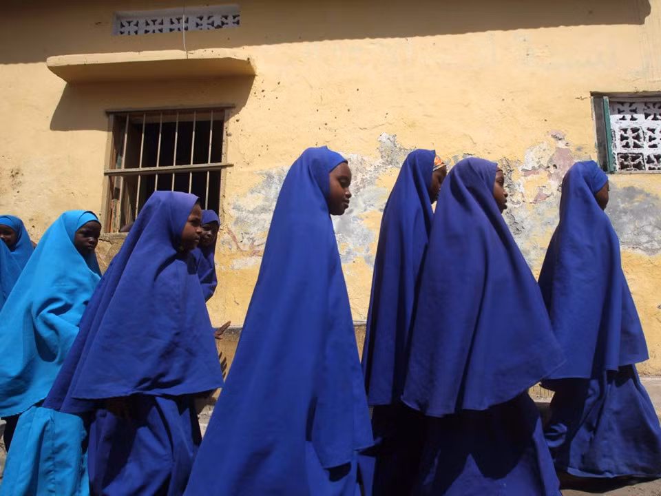 Học sinh Somalia đội khăn choàng đầu màu xanh, mặc trang phục phủ kín cơ thể, đi bộ đến trường tiểu học và trung học Bustaale ở Mogadishu.