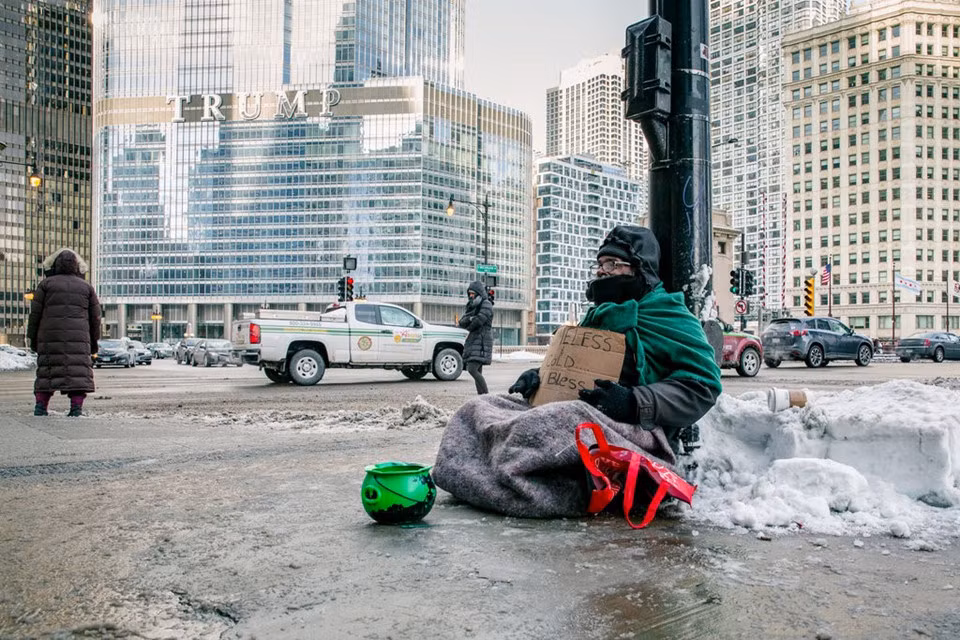 Andre Jones ngồi ở góc Michigan Avenue và Wacker Drive trong giá rét ở Chicago ngày 29/1, không xa con phố lấp lánh hàng hiệu Magnificent Mile. Với một cái vại màu xanh lá cây trước mặt, ông nói với New York Times ông đang cố xin đủ tiền cho căn phòng mà ông được phép trú tạm với giá 20 đô-la/đêm. “Gần đủ rồi, tin tôi đi, tôi sẽ xin đủ”, ông nói. Tấm bìa của ông viết “Không nhà và rét. Chúa phù hộ cho bạn”. “Anh không nên ở ngoài thế này”, một phụ nữ công sở nói với ông khi đi qua, hứa sẽ quay lại đưa tiền. Ảnh: New York Times.