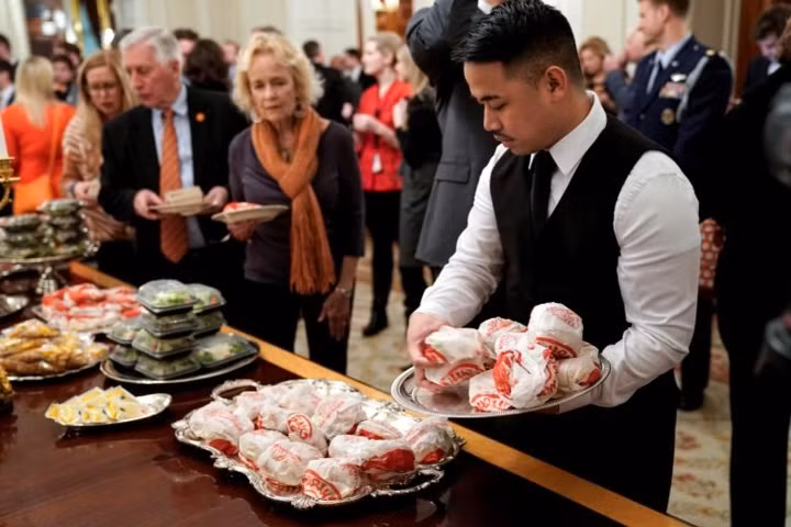 Nhân viên phục vụ đặt thêm bánh hamburger vào khay.