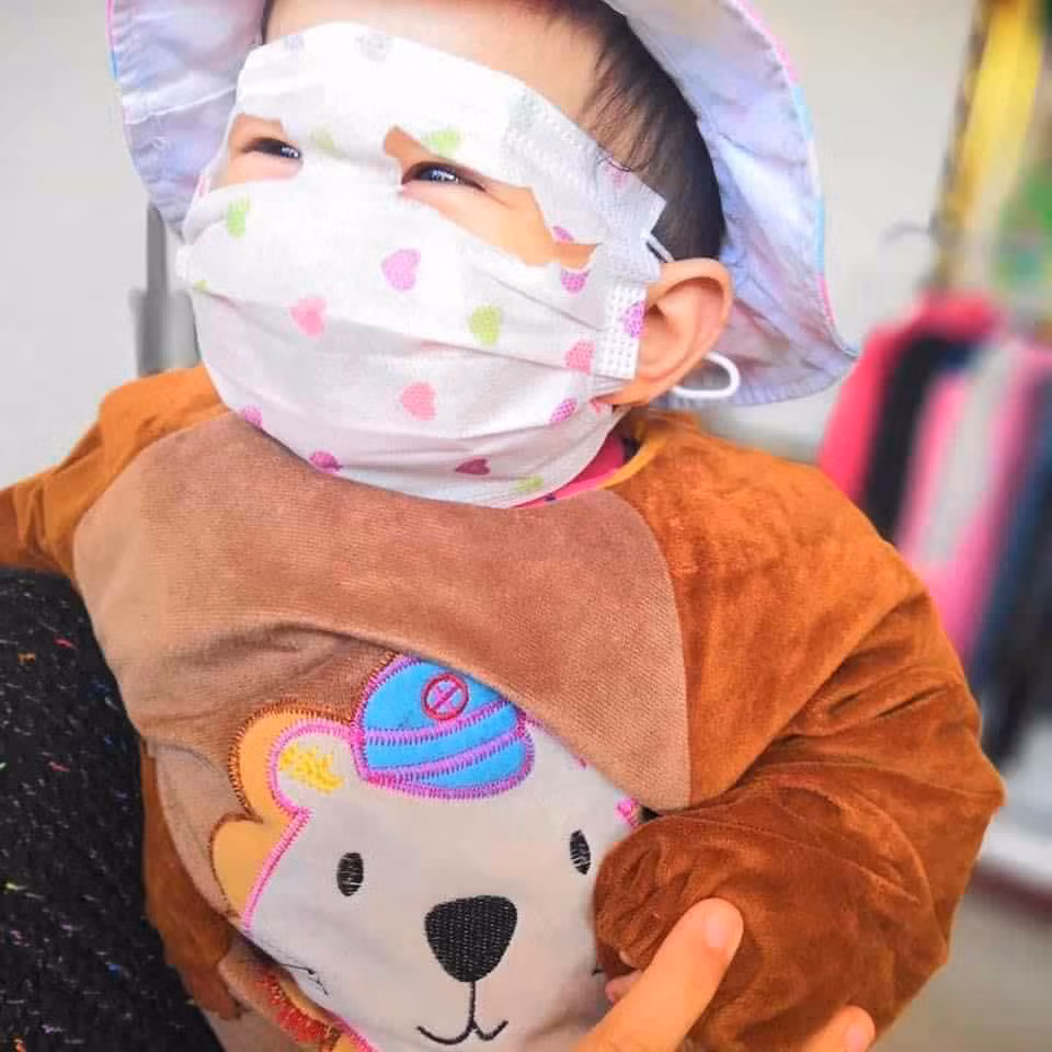Vì kích cỡ những chiếc khẩu trang quá to, chỉ đeo đơn thuần thì cũng đã che cả mặt với trán của các bé rồi nên các phụ huynh đã cắt thành những lỗ để lộ phần mắt của bé.