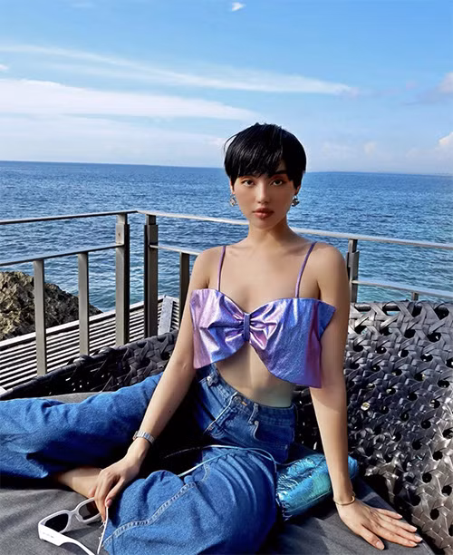 Khi đi du lịch biển, Khánh Linh lại chọn áo đính nơ kiểu hai dây để mix cùng quần jeans ống suông.