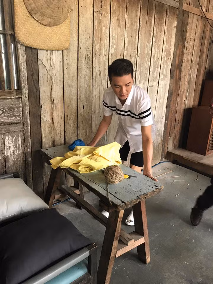 Trong hình ảnh, Mr Đàm mặc áo sơ mi ngắn tay kết hợp với quần short tối màu "cơ động" bê bàn ghế, đồ vật bố trí khung cảnh trước khi buổi họp báo diễn ra.