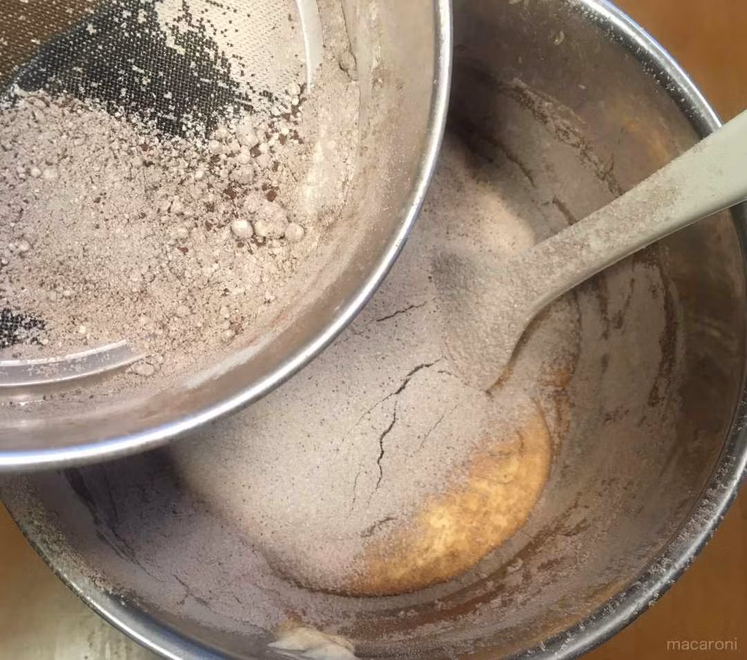 Chia bột ra làm 2 phần rồi rây từ từ vào âu, trộn đều, tránh bột ca cao lắng xuống đáy.