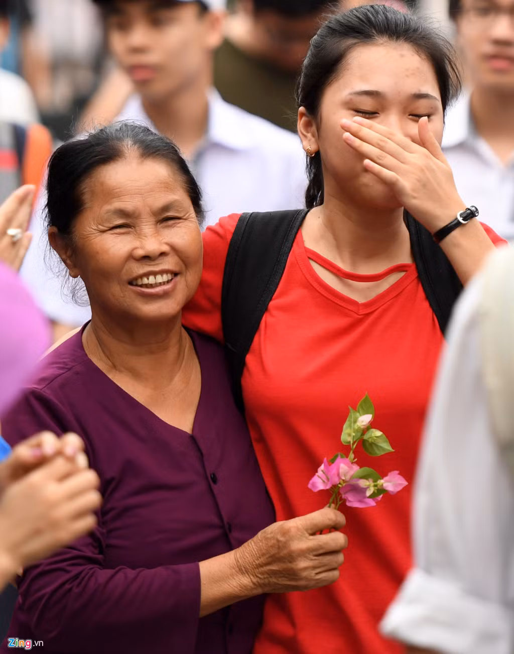 Trong số hàng trăm phụ huynh chào đón con em mình ngoài cổng trường THPT Yên Hoà sau giờ thi môn Toán, hình ảnh bà ngoại đón cháu nổi bật nhất. Nhiều người tò mò vây quanh đón xem.