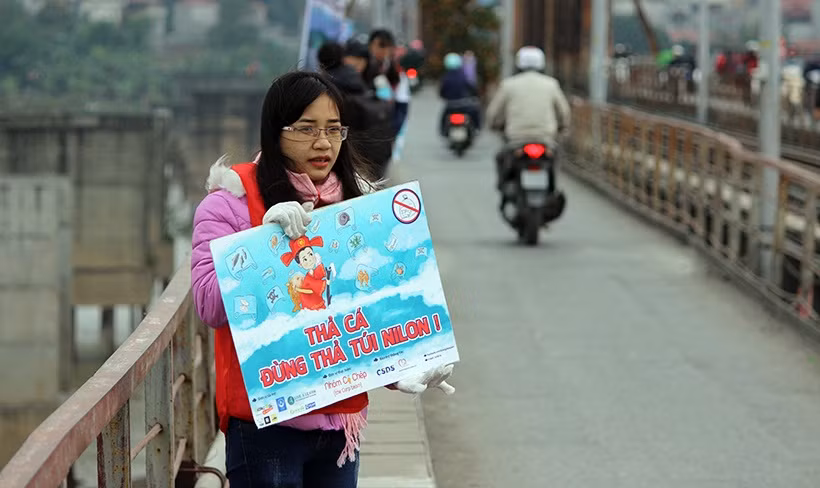 Một sinh viên tình nguyện mang theo thông điệp "thả cá đừng thả túi nilon" ở cầu Long Biên.