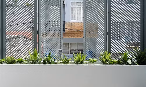 Mặt tiền ngôi nhà được thiết kế tích hợp vườn cây nhỏ. Hệ cửa sắt thiết kế dưới dạng các thanh lam chắn bao bọc toàn bộ trên và dưới ngôi nhà.
