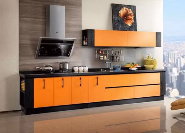 Nếu bạn yêu thích vẻ ngoài sáng bóng thì tủ bếp Acrylic là lựa chọn tuyệt vời. Đây cũng là loại vật liệu phổ biến của các loại tủ kệ ở những căn hộ cao cấp. Ở thiết kế này, sắc cam phối hợp với màu đen đã tạo nên cái nhìn mạnh mẽ, nổi bật. Bức tranh bông hoa với sắc màu “tông xuyệt tông” đặt ở tủ trên làm điểm nhấn mềm mại cho góc bếp.