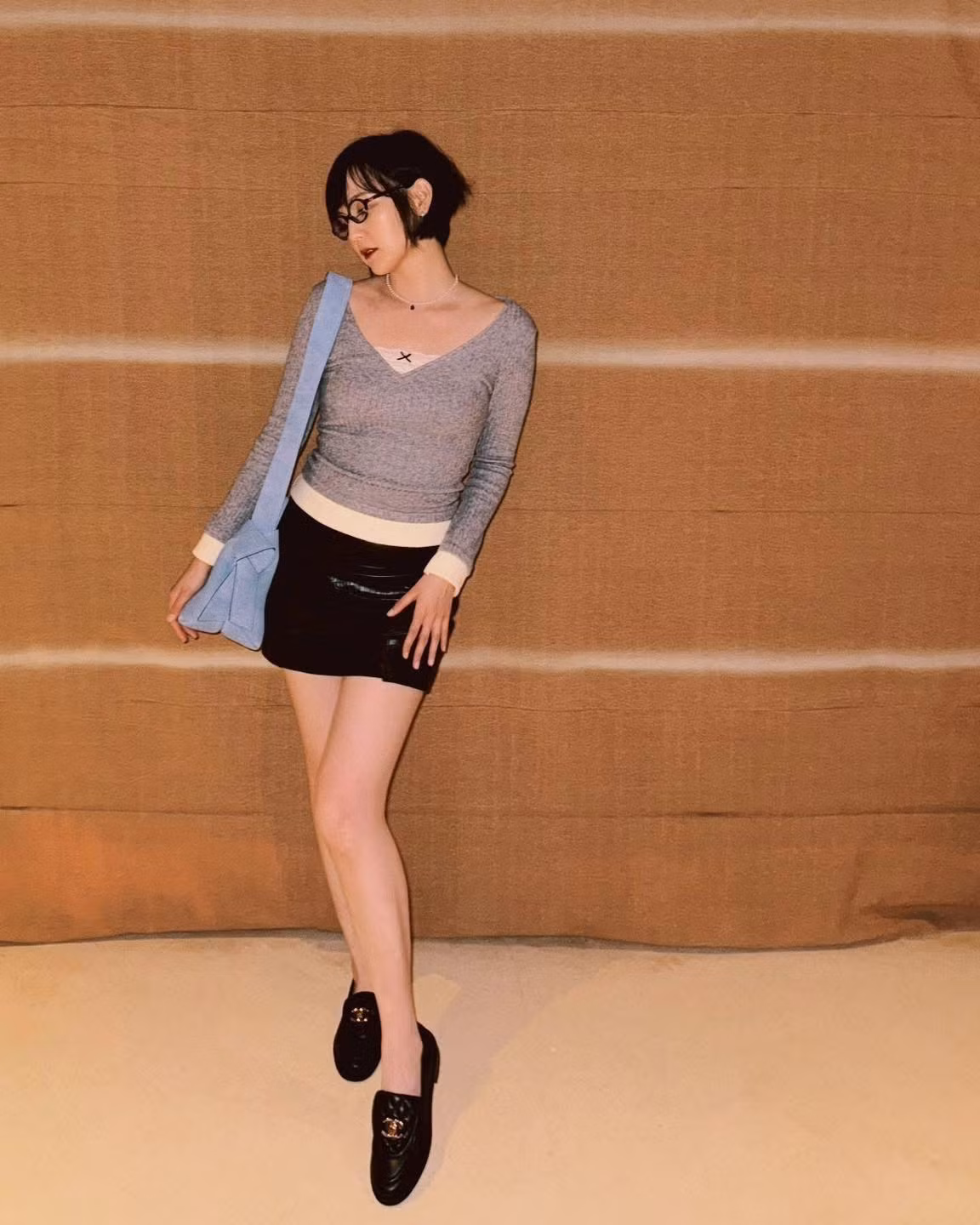 Điểm nhấn đáng chú ý chính là chiếc túi xách màu xanh pastel nhẹ nhàng – tạo nên sự tương phản thú vị với tổng thể trang phục.