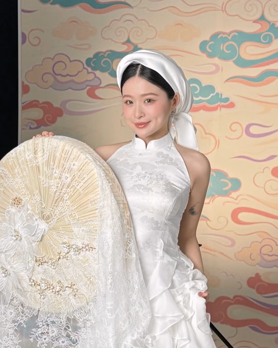 Thiết kế yếm trắng mang vẻ đẹp thanh lịch, dịu dàng nhưng đầy cuốn hút. Chiếc khăn lụa đội đầu kết hợp với quạt ren giúp Chao trông như một nàng tiểu thư đài các của thời xưa.