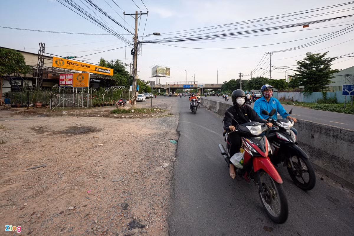 Trong khi đó, đoạn qua cầu vượt Đỗ Xuân Hợp (nút giao cao tốc TP.HCM - Long Thành - Dầu Giây), mặt đường đã được mở rộng, nhưng vẫn chưa thể kết nối. Trong ảnh, bên phải là làn xe máy hướng về xa lộ Hà Nội chỉ rộng gần 2 m, trong khi bên trái vẫn trải đá dăm, cỏ dại mọc và các trụ điện nơi đây chưa được di dời.