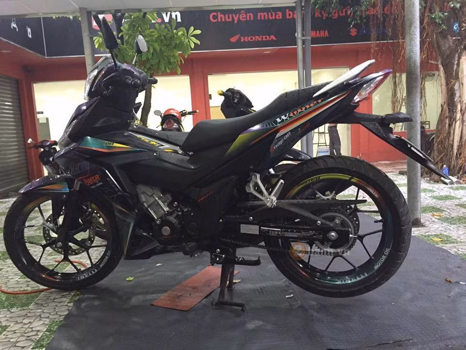 Chiếc Winner 150 của chủ nhân tại Sài Gòn độ dàn tem đấu với màu sơn chuyển màu qua mọi góc nhìn. Điểm nhấn của xe chính là tông màu xanh nổi bật kết hợp với màu đen tuyền đi kèm một số đồ chơi đơn giản.