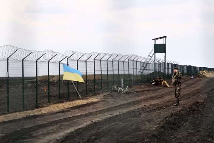 Một sĩ quan canh gác biên giới Ukraine đứng gần một lá quốc kỳ nước này được treo lên hàng rào biên giới Nga - Ukraine gần Hoptivka, khu vực Kharkiv ở phía đông Ukraine ngày 18/4/2015.
