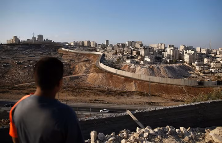 Một bức ảnh chụp ngày 18/10/2016 cho thấy một chàng trai Palestine đang nhìn về phía trại tị nạn Shuafat của Palestine (phải) đằng sau bức tường biên giới gây tranh cãi của Israel.