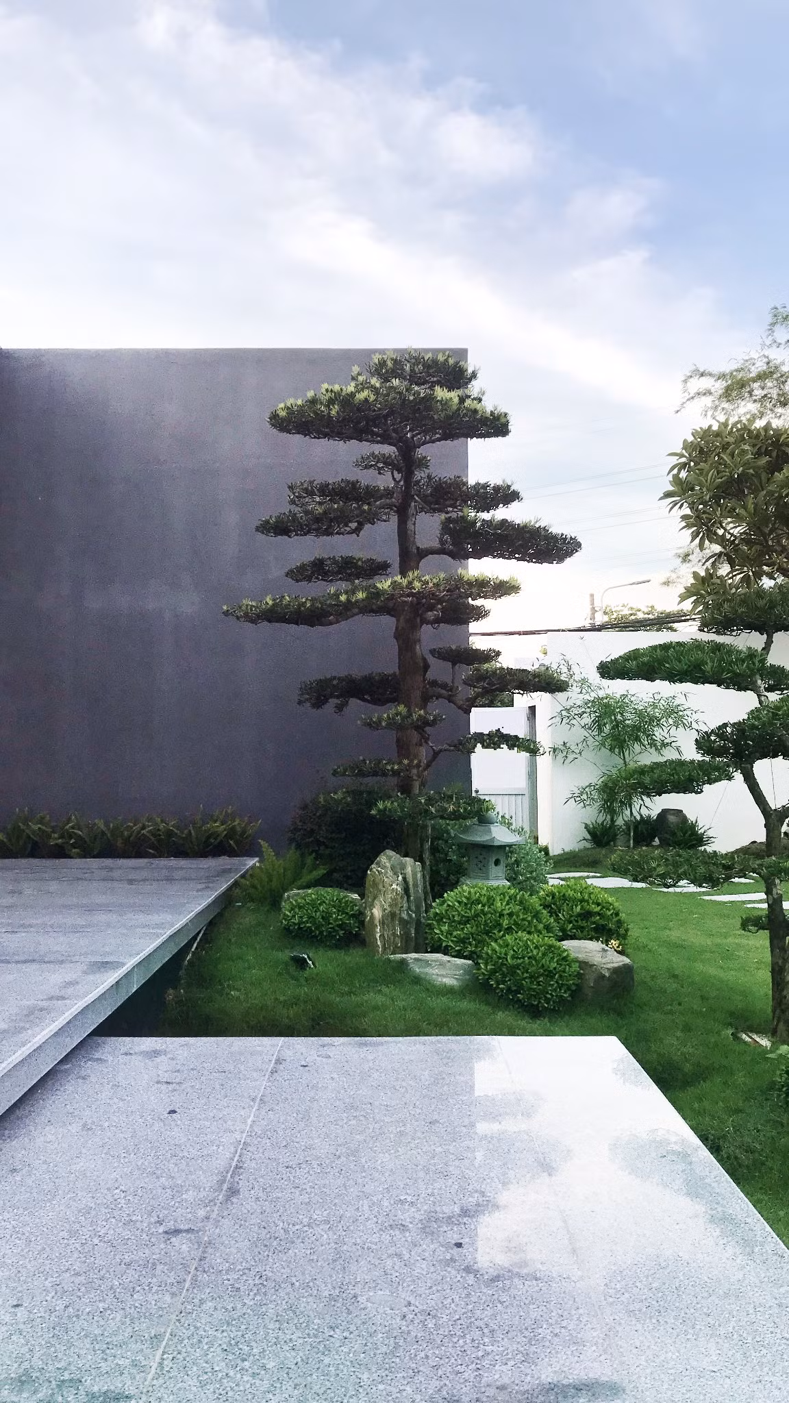 Bên ngoài căn nhà rợp bóng mát với thảm cỏ xanh mướt và hệ cây cảnh được cắt tỉa dẹp mắt.