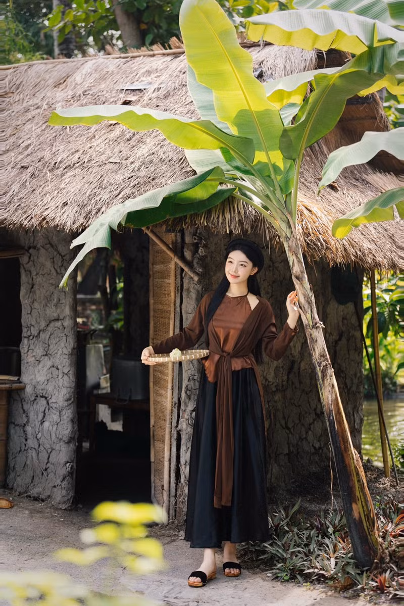 Lọ Lem chọn áo tứ thân màu nâu trầm kết hợp yếm đào, tóc buông xõa tự nhiên, trang điểm nhẹ nhàng phù hợp với không gian làng quê yên bình.